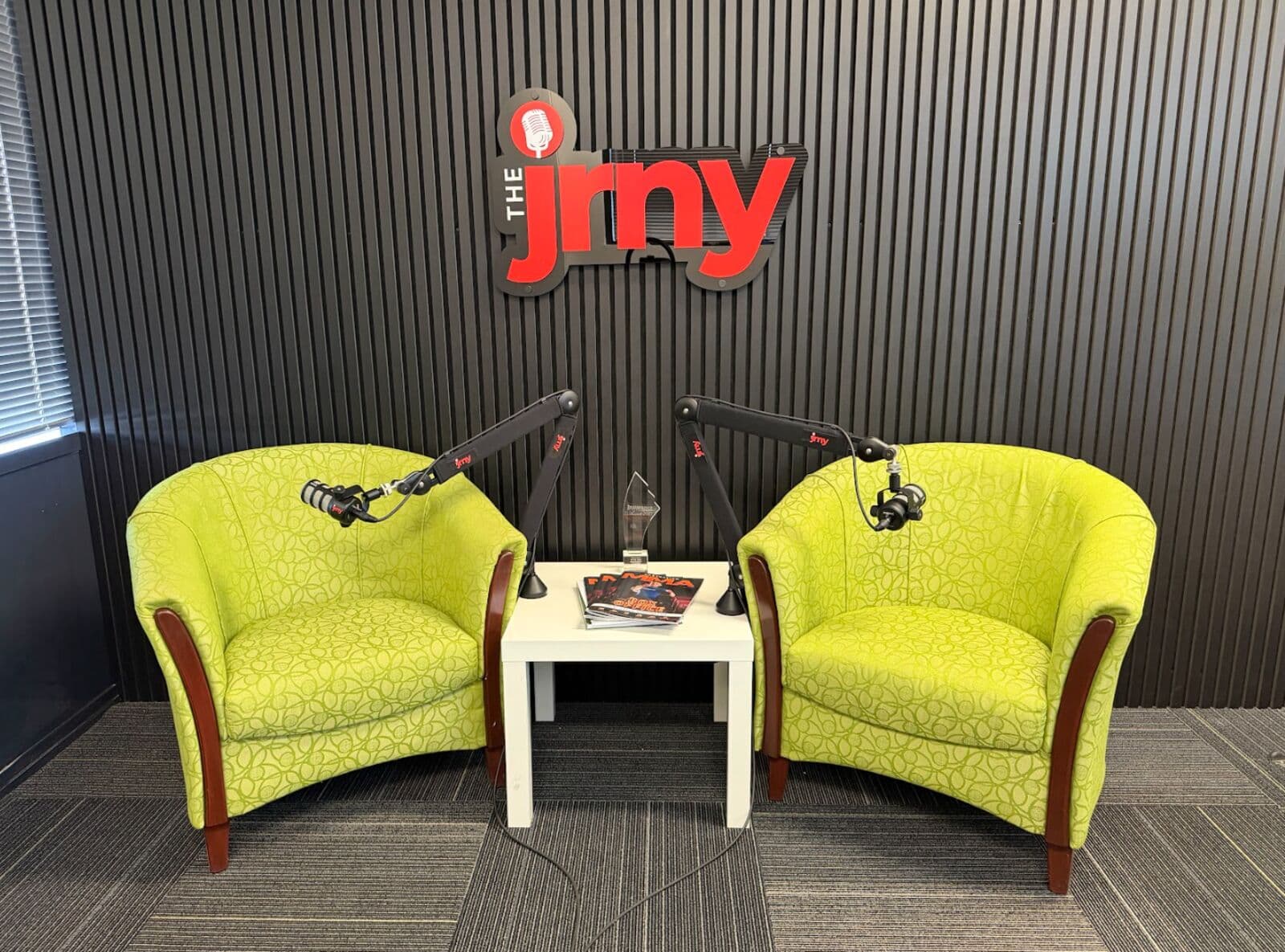 The JRNY studio with two green tub chairs, boom microphones and the the jrny wall sign